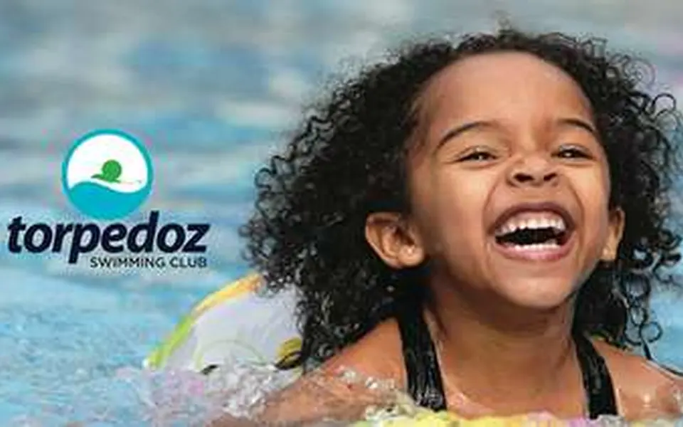 Laughing child in a pool beside the Torpedoz Swimming Club logo
